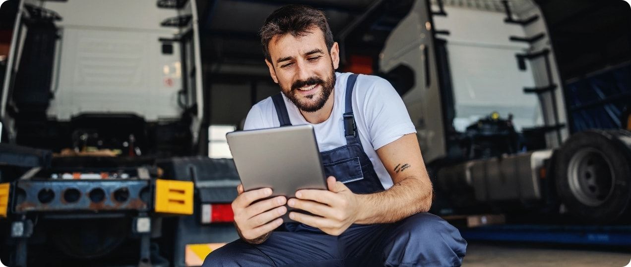 A man looking at a tablet while sitting near two semi cabs