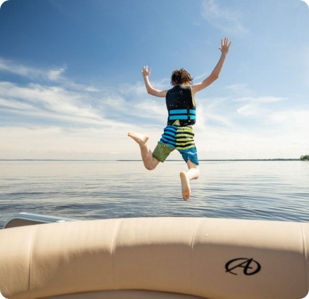 A boy jumps off the back of a boat into a lake. 