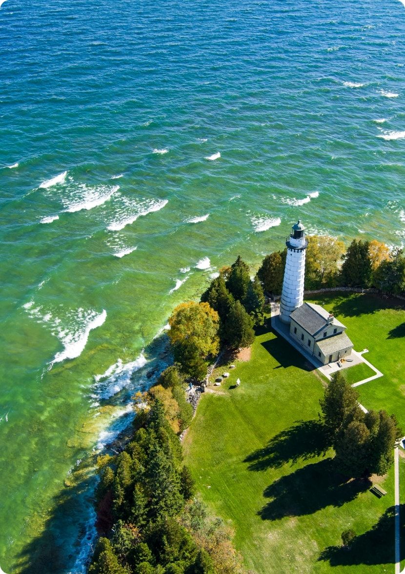 An ariel view of a lighthouse on the edge of Lake Michigan. 
