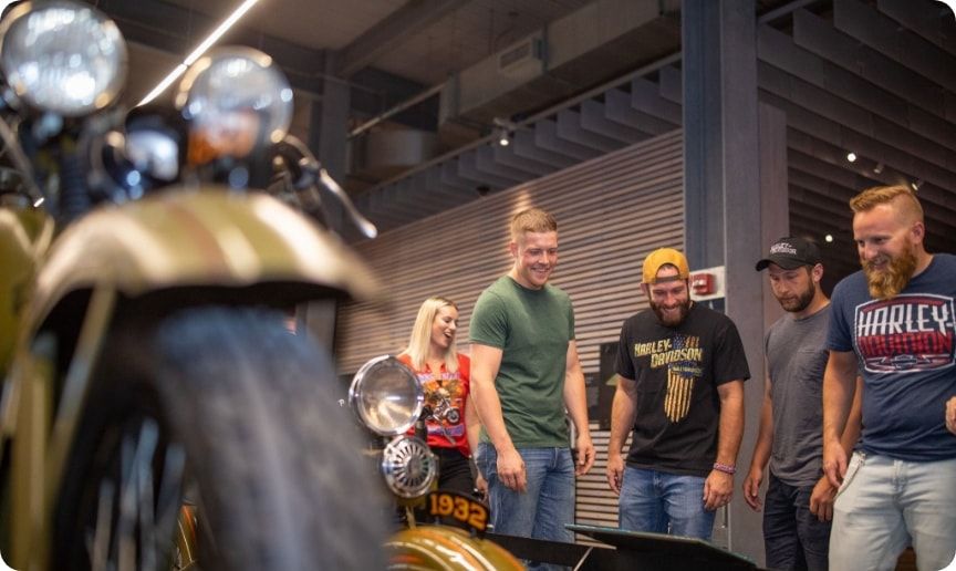 A group of friends reading about a motorcycle at the Harley-Davidson museum.  
