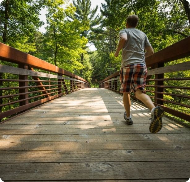 A man jogging on a path that crosses a bridge. 