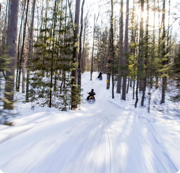 Two people on a snowmobile along a snowy path.