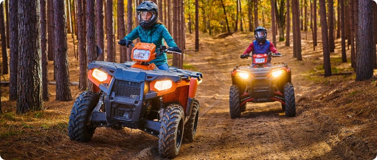 Two folks riding ATVs on a path in the woods.